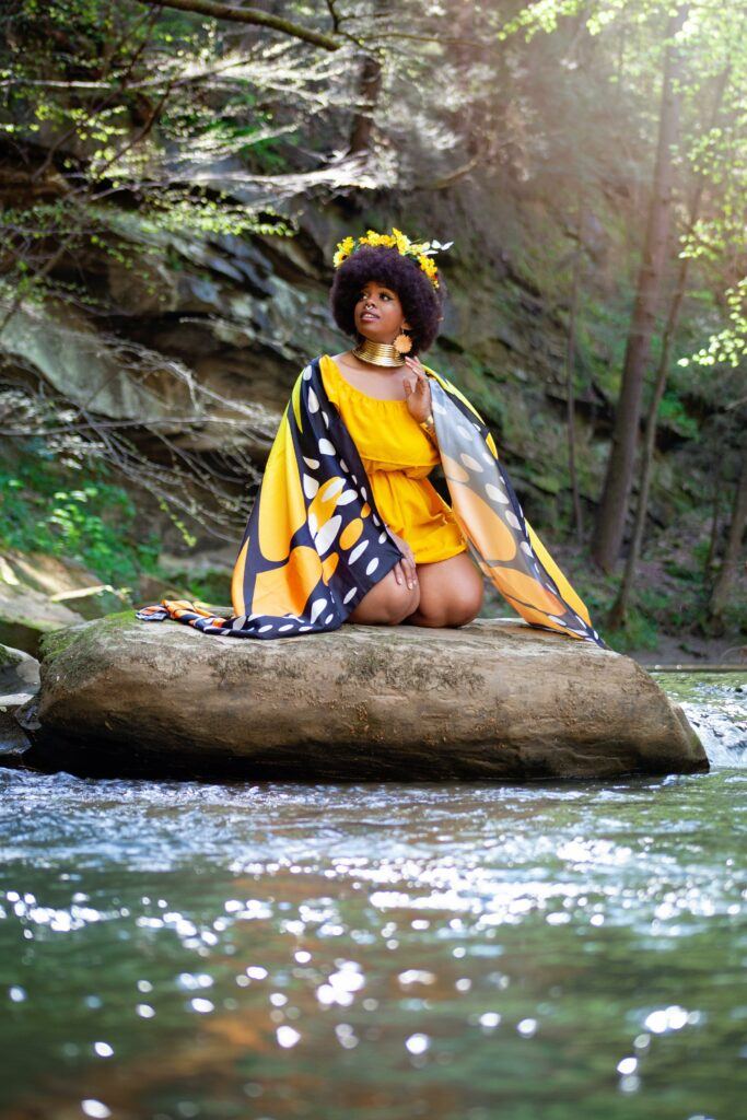 Black woman in yellow dress with butterflying wing sleeves for Black Fae Day
