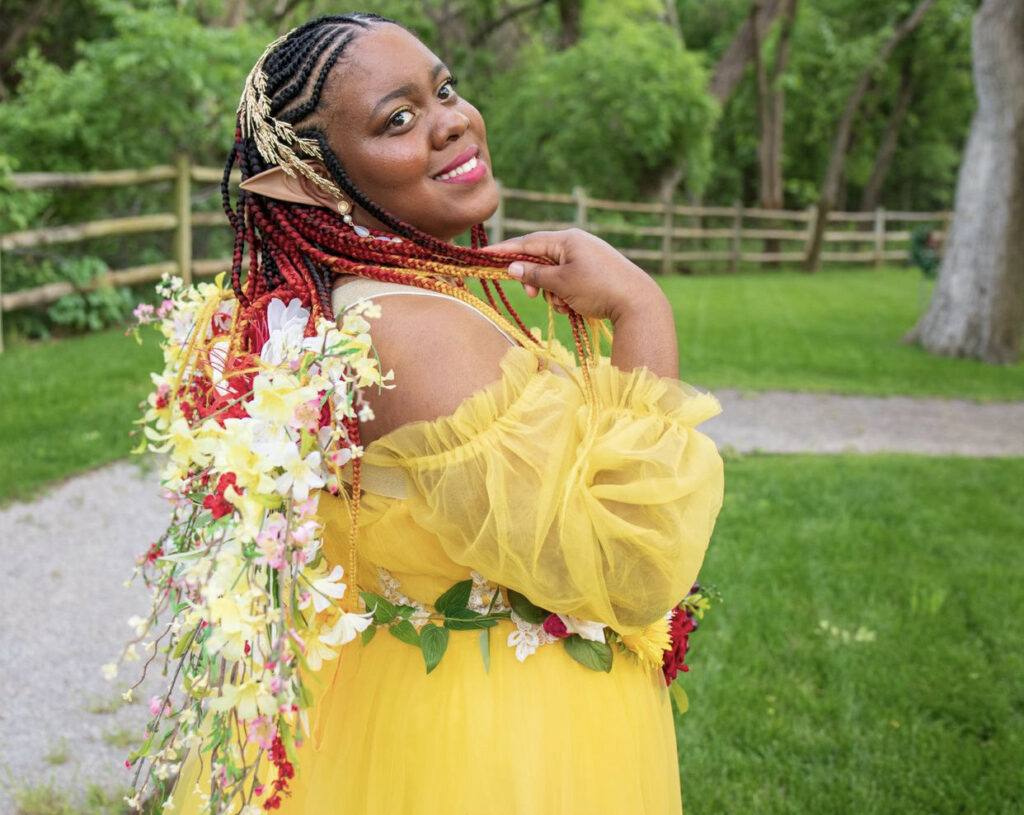 Picture of a black woman with flowers in her hair and yellow dress for Black Fae Day